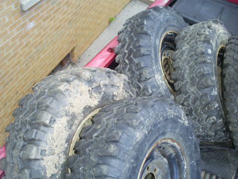 1994 Ford F-250 - Several large, mud-caked off-road tires are piled up in the cargo area of a vehicle.