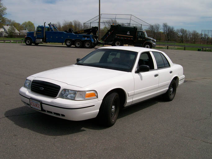 White 1999 Ford Crown Victoria parked in lot with tow truck and garbage truck behind