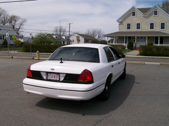 White Ford Crown Victoria sedan from rear three-quarter with steel wheels and trunk antenna
