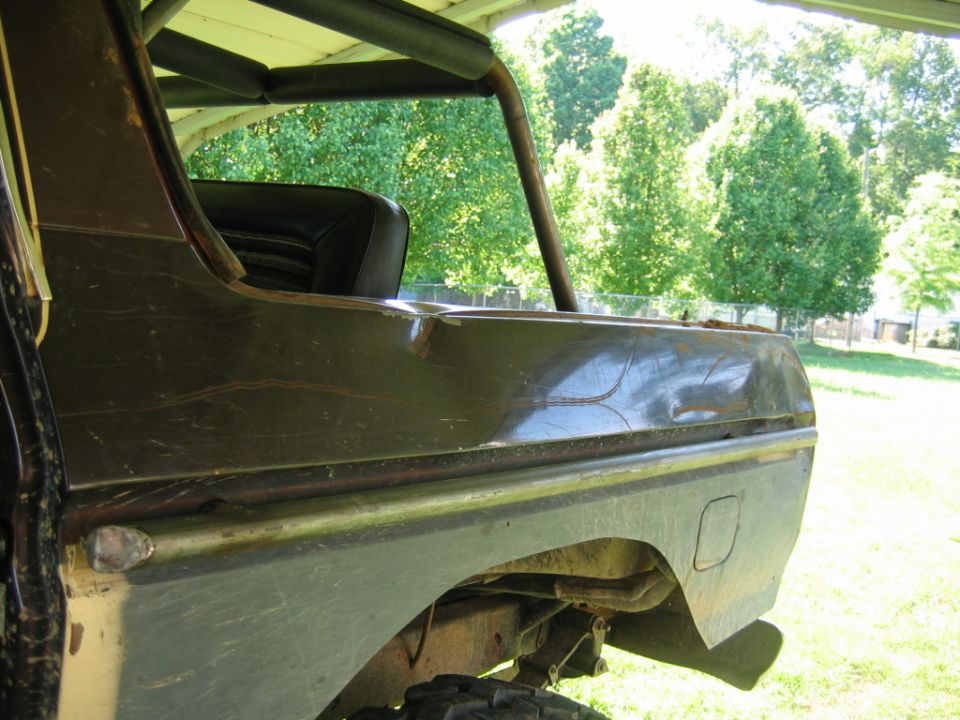 rear quarter panel of a pickup truck with a dent and some scratches, roll bar visible inside