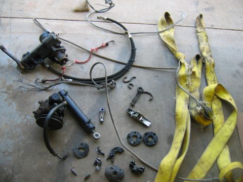 1992 Ford Mustang - Various automotive parts, including a steering rack, hydraulic cylinder, cables, and lifting straps, are laid out on a concrete surface.