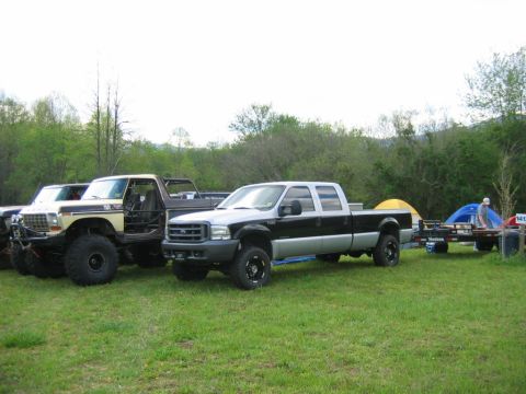 1992 Ford Mustang - Two pickup trucks are parked on grass, one towing a trailer with camping gear.