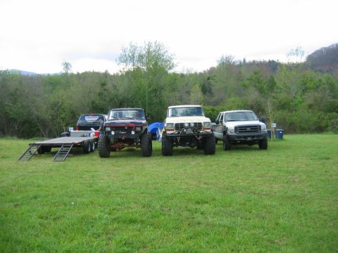 1992 Ford Mustang - A collection of modified trucks and a trailer are parked on a grassy field with trees in the background.