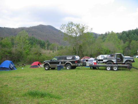 1992 Ford Mustang - Camping scene with two trucks and a trailer, set against a backdrop of rolling hills and trees.