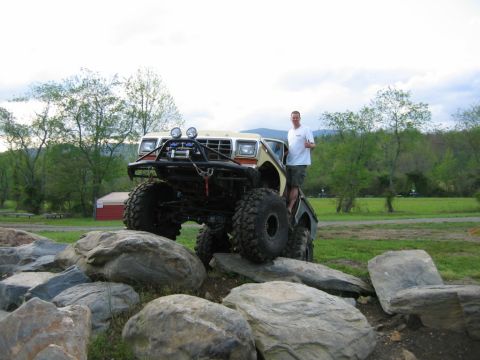 1992 Ford Mustang - A man stands on a heavily modified truck navigating a rocky obstacle course.