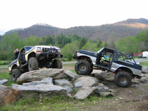 1992 Ford Mustang - Two heavily modified trucks navigate a rocky obstacle course with a mountainous backdrop.