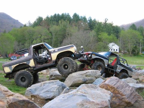 1992 Ford Mustang - Modified off-road trucks traverse a challenging rocky obstacle course in a natural setting.