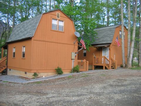 1992 Ford Mustang - Two rustic cabins, each adorned with an American flag, are situated amongst trees.