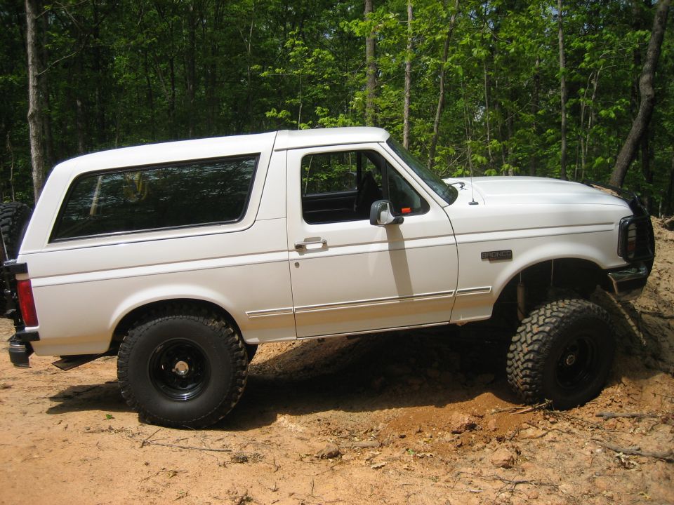 White lifted Ford Bronco on dirt mound in a wooded area