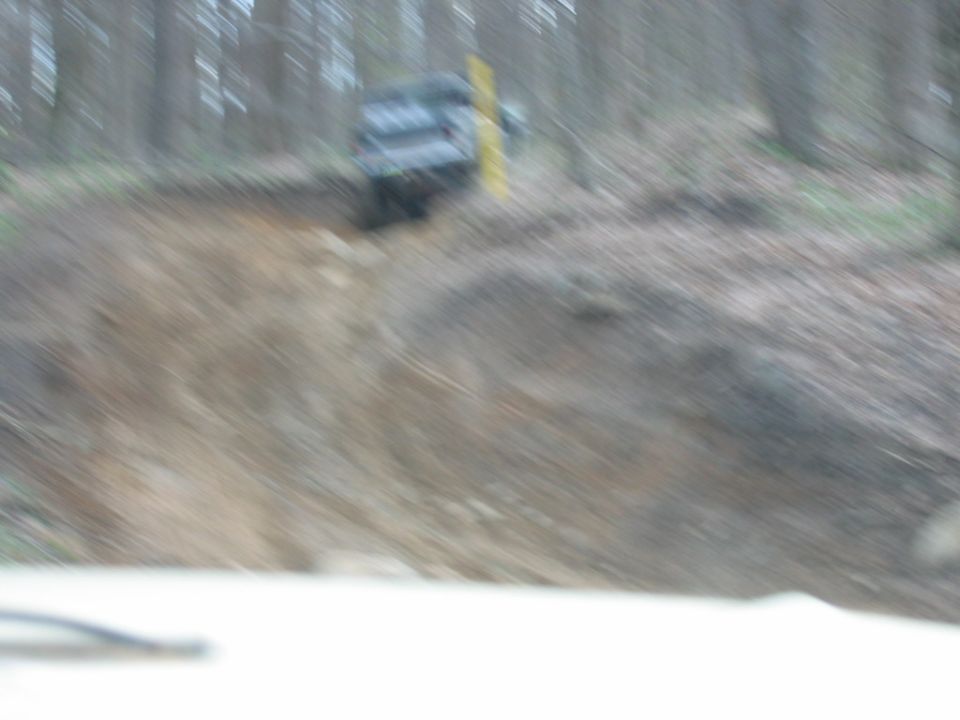 dark off-road vehicle driving down a steep, muddy hill in a wooded area