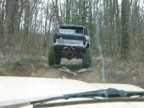 1992 Ford Mustang - A lifted off-road vehicle navigates a challenging trail through a wooded area.