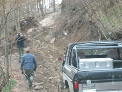 1992 Ford Mustang - Off-road vehicle navigates a rocky, wooded trail with two people walking ahead.