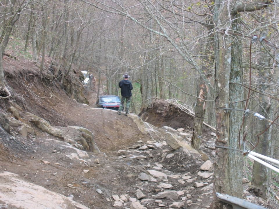 Two off-road vehicles navigate a steep, rocky trail through a wooded area