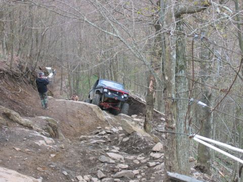1992 Ford Mustang - Off-road vehicles tackle a challenging, rocky trail in a wooded environment.