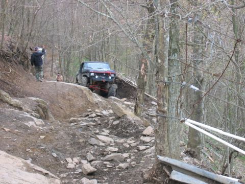 1992 Ford Mustang - An off-road vehicle navigates a challenging, rocky terrain in a wooded area.