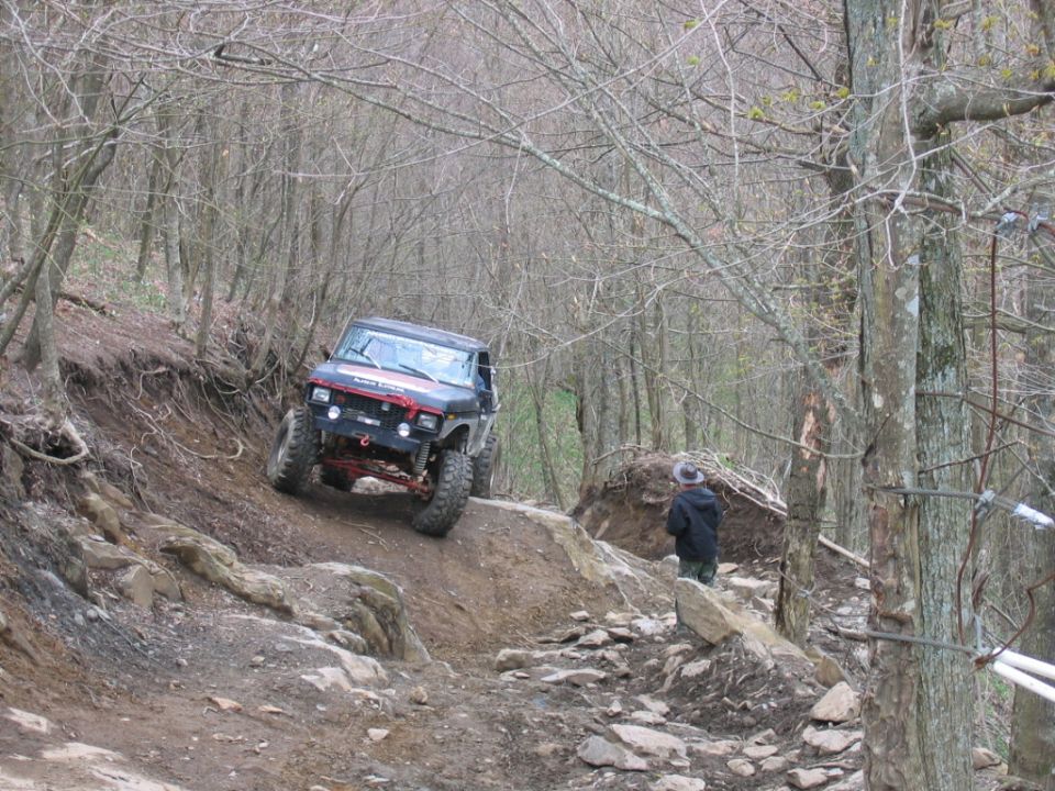 Black off-road vehicle navigating a steep, rocky trail with trees on either side