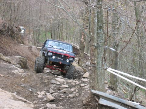 1992 Ford Mustang - An off-road vehicle navigates a challenging rocky path in a wooded area, with another vehicle ahead.
