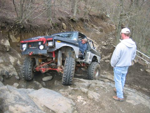 1992 Ford Mustang - A heavily modified pickup truck tackles a challenging rocky terrain with a person watching.
