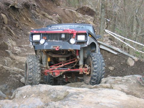 1992 Ford Mustang - A heavily modified off-road truck tackles a challenging rocky trail with its front end prominently displayed.