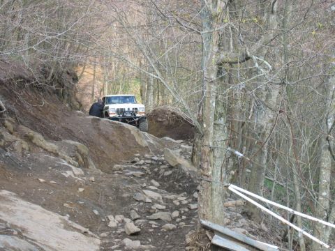 1992 Ford Mustang - A white off-road truck is seen on a challenging, rocky trail in a wooded area.