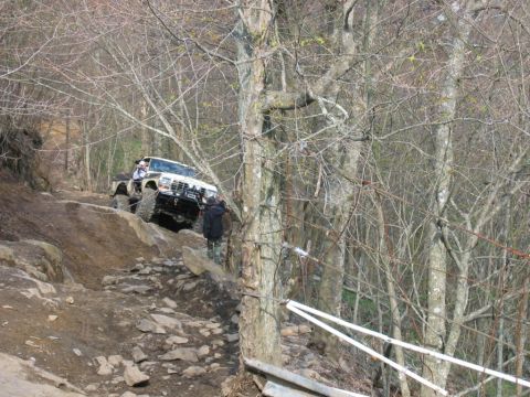 1992 Ford Mustang - An off-road vehicle navigates a challenging, rocky trail through a wooded area.