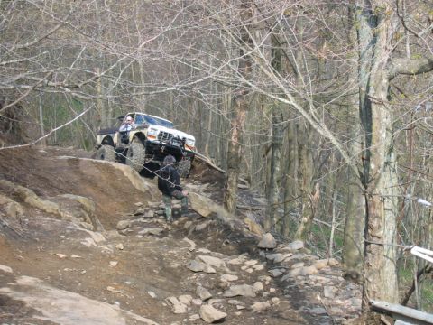 1992 Ford Mustang - A modified off-road truck navigates a challenging, rocky trail through a wooded area.