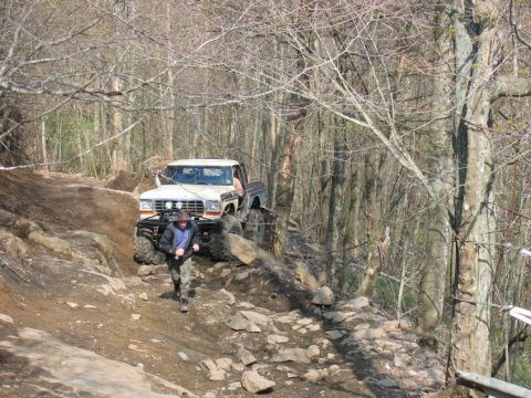 1992 Ford Mustang - A modified 1979 Ford F-Series pickup truck tackles a challenging off-road course with a person walking nearby.