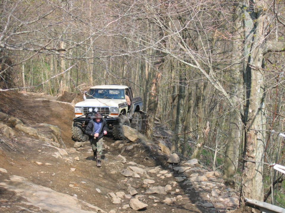 White 1979 Ford F-Series pickup truck with off-road modifications navigating a rocky trail