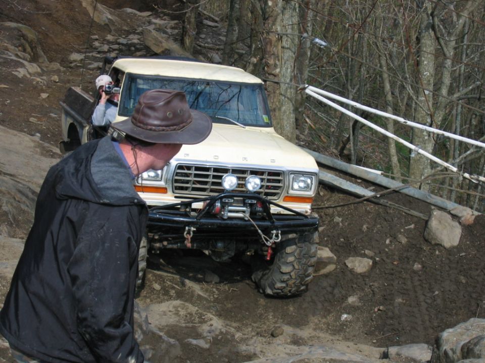 Off-road pickup truck with winch on rocky trail. Person in hat in foreground