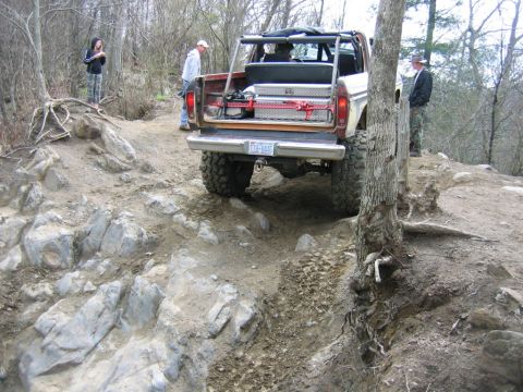 1992 Ford Mustang - A modified off-road vehicle tackles a challenging rocky incline with spectators observing.