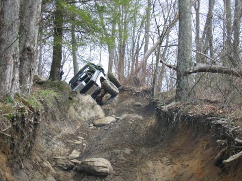 1992 Ford Mustang - An off-road vehicle navigates a steep, muddy, and rocky trail through a forest.