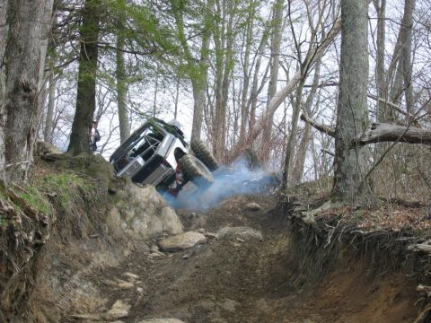 1992 Ford Mustang - An off-road vehicle navigates a challenging rocky incline, kicking up blue smoke as it ascends.