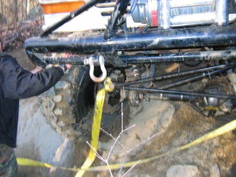 1992 Ford Mustang - A person is securing a tow strap to the front of an off-road vehicle, highlighting its winch and suspension system.