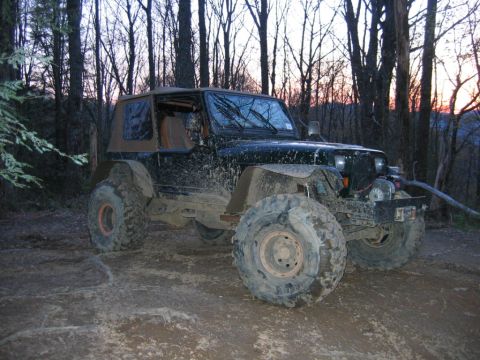 1992 Ford Mustang - A heavily muddied black Jeep Wrangler sits off-road, its large tires suggesting it's ready for challenging terrain.