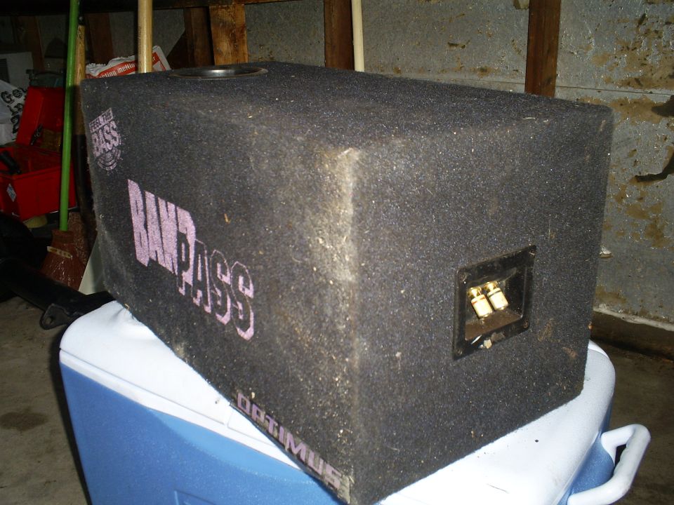 Car subwoofer with 'BANDPASS' and 'OPTIMUS' text, sitting on a cooler