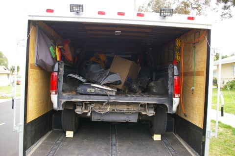 1986 Ford Bronco - Rear view of a pickup truck's bed filled with various parts, parked inside a trailer.