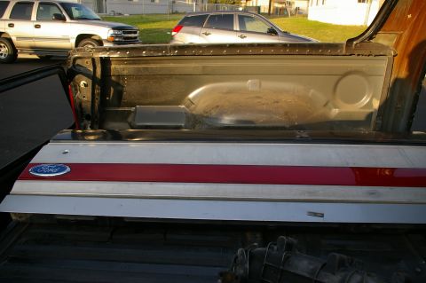 1986 Ford Bronco - The Ford emblem is visible on the tailgate of a truck, with other vehicles parked nearby.
