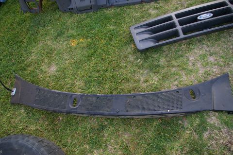 1986 Ford Bronco - A Ford grille and dashboard trim piece are laid out on the grass.
