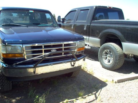 1995 Ford Bronco - Two Ford trucks, a blue F-Series and a black pickup, are parked side-by-side.