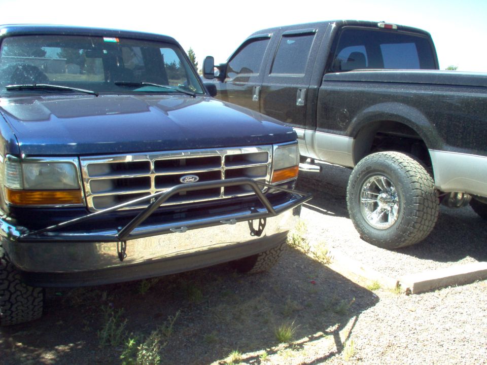 Front view of a blue Ford F-Series truck with a chrome grille and brush guard, parked next to a black pickup truck