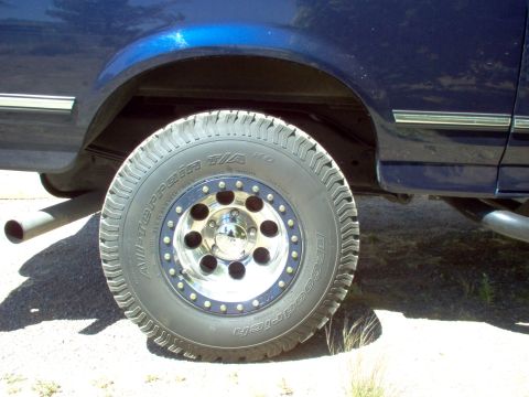 1995 Ford Bronco - Close-up of a blue SUV's rear wheel and fender area, showing off-road tires and custom rims.