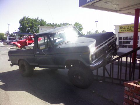 1995 Ford Bronco - Pickup truck with a red ATV in the bed is parked on a ramp next to a building.