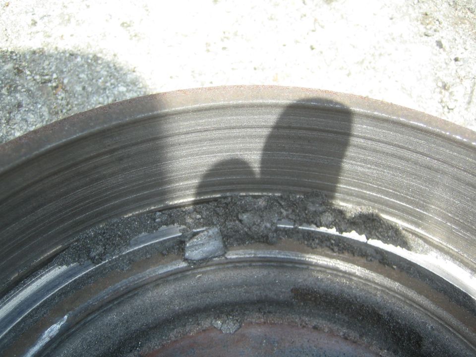 Close-up of a damaged brake rotor with chunks missing from the edge