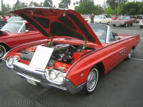 1990 Ford Bronco - red 1960s Ford Thunderbird convertible with wire wheels and open hood displaying an info card at a car show.
