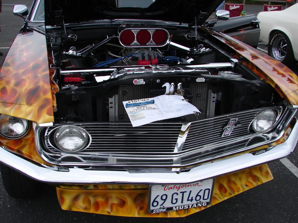 Black 1969 Ford Mustang with flame paint, hood open, chrome grille, and California license plate '69 GT460'