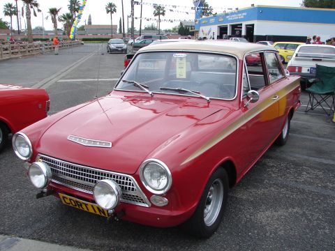 1992 Ford Taurus - A vintage Ford Cortina is parked in a lot with other vehicles and palm trees in the background.