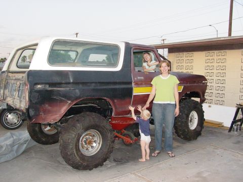 1979 Ford Bronco - A modified 1979 Ford Bronco with a distinctive yellow stripe and lifted suspension is shown with two women and a child. Another vehicle is…