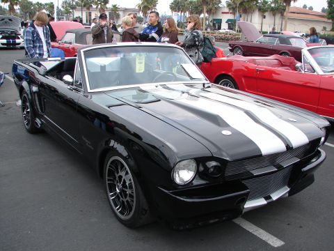 1992 Ford Taurus - A black 1965 Ford Mustang convertible with racing stripes is parked at an outdoor car show.