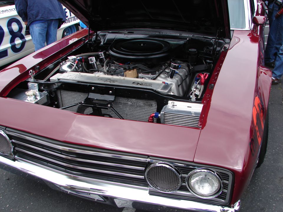 Maroon classic car with hood open showing engine, radiator, and intercooler. Another car with a large number '28' is visible behind it