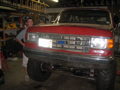 1990 Ford Bronco - A red 1990 Ford Bronco is shown in a garage with a person standing beside it, highlighting its modified suspension.